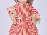 une poupée à l'ancienne, vêtue d'une robe rayée rouge et blanche et de chaussures rouges