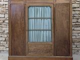 une vieille armoire en bois avec une porte vitrée, sur fond de mur de briques