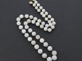 un collier de perles blanches muni d'un fermoir doré, sur fond noir