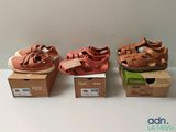 trois paires de chaussures pour bébé dans leurs boîtes, posées sur une surface blanche