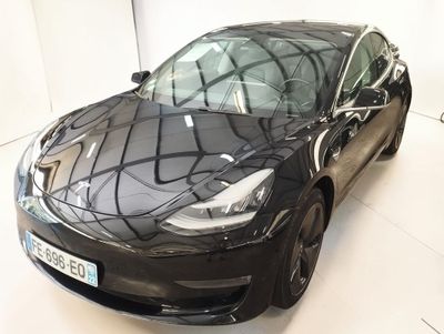 une photo d'une Tesla Model 3 noire garée dans une pièce blanche