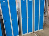 Plusieurs casiers bleus sont alignés contre un mur de briques dans un entrepôt