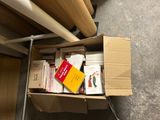 une boîte en carton remplie de livres et de papiers, posée par terre