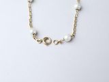 a gold chain bracelet with white pearls on a white background