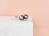 a black pearl and diamond ring sitting on top of a white marble block