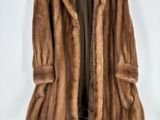 un manteau de fourrure marron suspendu à un cintre sur fond blanc