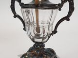 an antique silver plated glass teapot with a wooden spoon on a stand