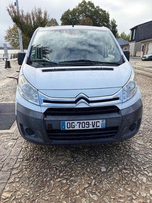 the front of a silver van parked on a cobblestone road