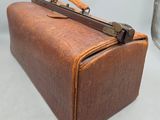 une valise en cuir marron posée sur une surface blanche, à côté d'un conteneur métallique