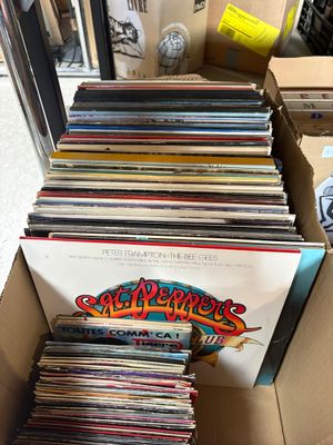 une boîte en carton ouverte, remplie de disques de toutes sortes, posée sur une table