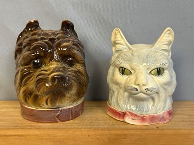 two ceramic cats sitting on a shelf next to each other