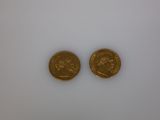 two gold coins sitting on top of each other on a white surface