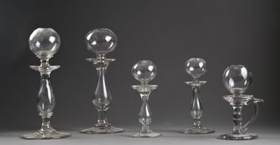 six bougeoirs en verre transparent sont alignés sur un fond gris