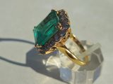 a close up of a ring with a green stone surrounded by black diamonds