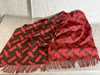 une écharpe rouge et noire posée sur un canapé blanc, avec une chaise blanche en arrière-plan