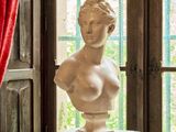 un buste de femme assise sur un socle devant une fenêtre