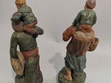 deux figurines représentant des personnes portant des paniers, posées sur une surface blanche