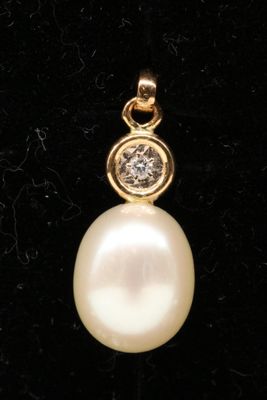 a close up of a pearl and diamond pendant on a black velvet surface
