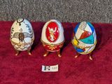 three decorated eggs sitting on top of a red cloth covered table