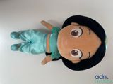 une peluche représentant une petite fille portant un chapeau noir et un pantalon bleu