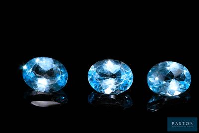 three blue topazte gems sit side by side on a black surface