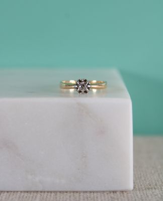 une image représentant une bague en diamant posée sur un bloc de marbre blanc