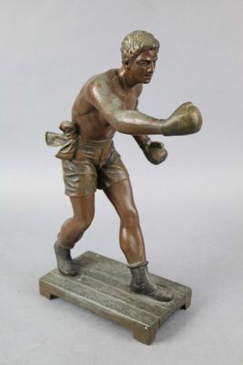 statue en bronze représentant un garçon portant un gant de boxe, posée sur un socle en bois