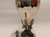 a silver vase with a red lid next to a silver cup