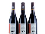 three bottles of red wine sitting next to each other on a white surface