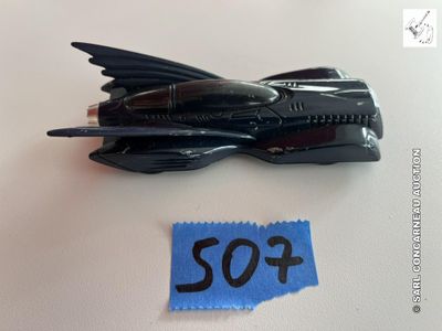une Batmobile miniature noire posée sur une surface blanche, à côté d'une feuille de papier bleue