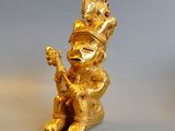 gold figurine of a man with a guitar sitting on a rock