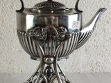 a silver tea pot on a stand on a table