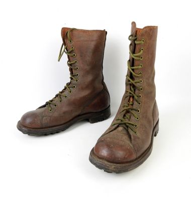 une paire de bottes marron ornées de lacets verts, posées sur une surface blanche