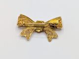 a close up of a gold bow brooch on a white surface