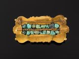 a gold broochle with turquoise beads on a black surface