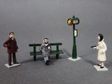 three figurines of people sitting on a bench next to a street sign