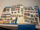 de nombreux timbres posés sur une table, à côté d'un classeur bleu