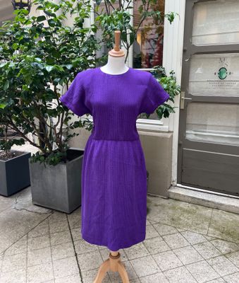 une robe violette posée sur un mannequin devant un immeuble