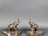 pair of bronze elephants on marble bases on a gray background