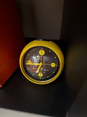 a yellow clock sitting on a black shelf next to a red box