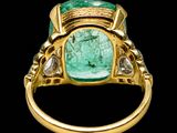 a close up of a ring with a green stone surrounded by diamonds