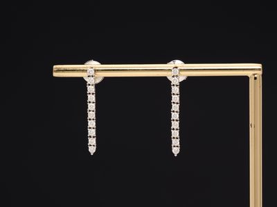 une paire de boucles d'oreilles en diamant posées sur un socle en or, sur fond noir