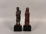 deux petites figurines en bois représentant un homme et une femme, posées sur des socles noirs
