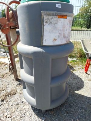 un grand réservoir gris muni d'un couvercle vert, posé sur le bord de la route