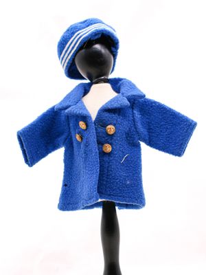 une poupée vêtue d'un manteau bleu et d'un chapeau, posée sur un mannequin