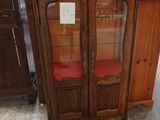 une armoire en bois avec une porte vitrée et une chaise rouge
