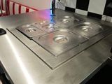 un plan de travail en acier inoxydable équipé de quatre feux, dans une cuisine aux murs à carreaux
