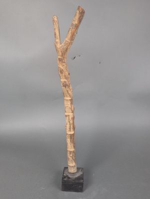 sculpture représentant une branche d'arbre sur un socle noir, avec un fond gris