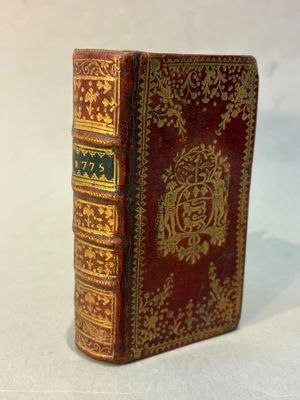 an old book with gold and red cover sitting on a white surface