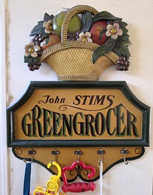 a sign that says john stim greengrocer with a basket of fruit hanging on the wall